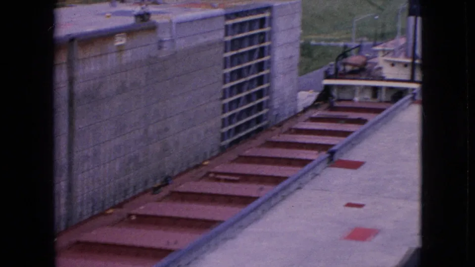 Elevated 1964 view of the Niagara Falls power facility showing a concrete wall with a grated section, red deck panels, paved ground, and equipment beyond the structure.