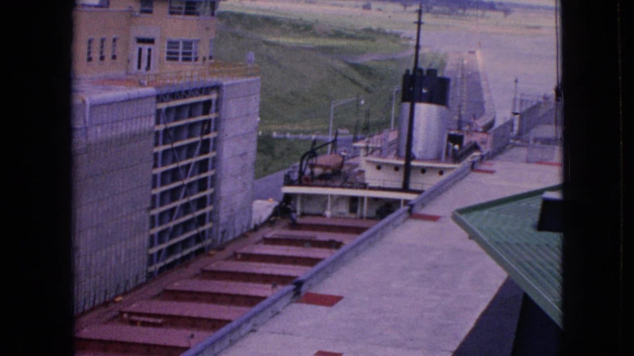 1964 Niagara Falls, New York home-movie frame showing an elevated view into a concrete lock area with red metal steps and a small white tugboat near the chamber.