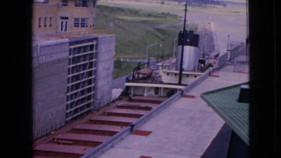 1964 Niagara Falls, New York home-movie frame showing an elevated view into a concrete lock area with red metal steps and a small white tugboat near the chamber.