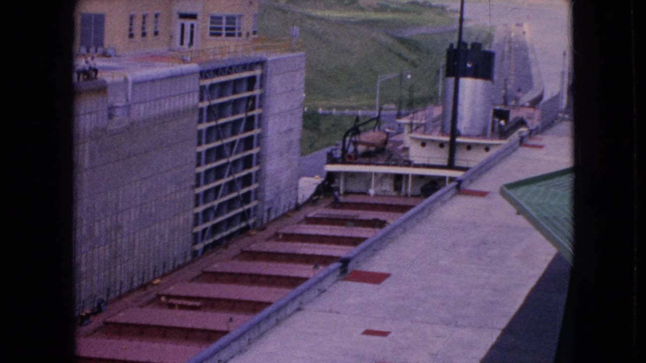Concrete lock chamber with red metal steps, railings, and a small tugboat near the far end.