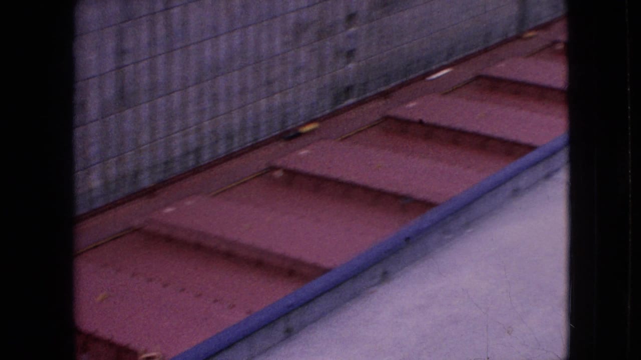 1964 Niagara Falls home-movie frame looking down at a red-painted dock or vessel surface beside a tall concrete wall.