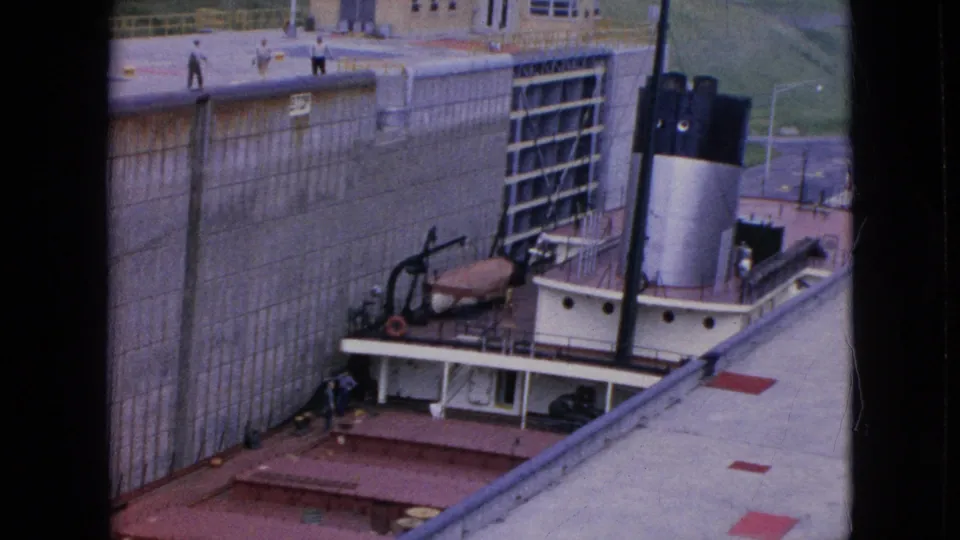 Niagara Falls, New York, 1964 frame showing the tugboat squeezed along the lock wall beneath a gate and walkway, with distant people visible above.
