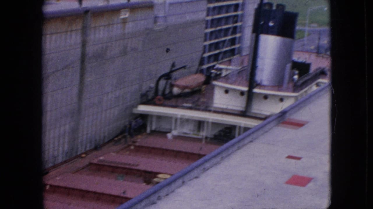 1964 8mm frame from Niagara Falls, New York, showing a tugboat with a black stack beside a concrete canal lock wall and gate structure.