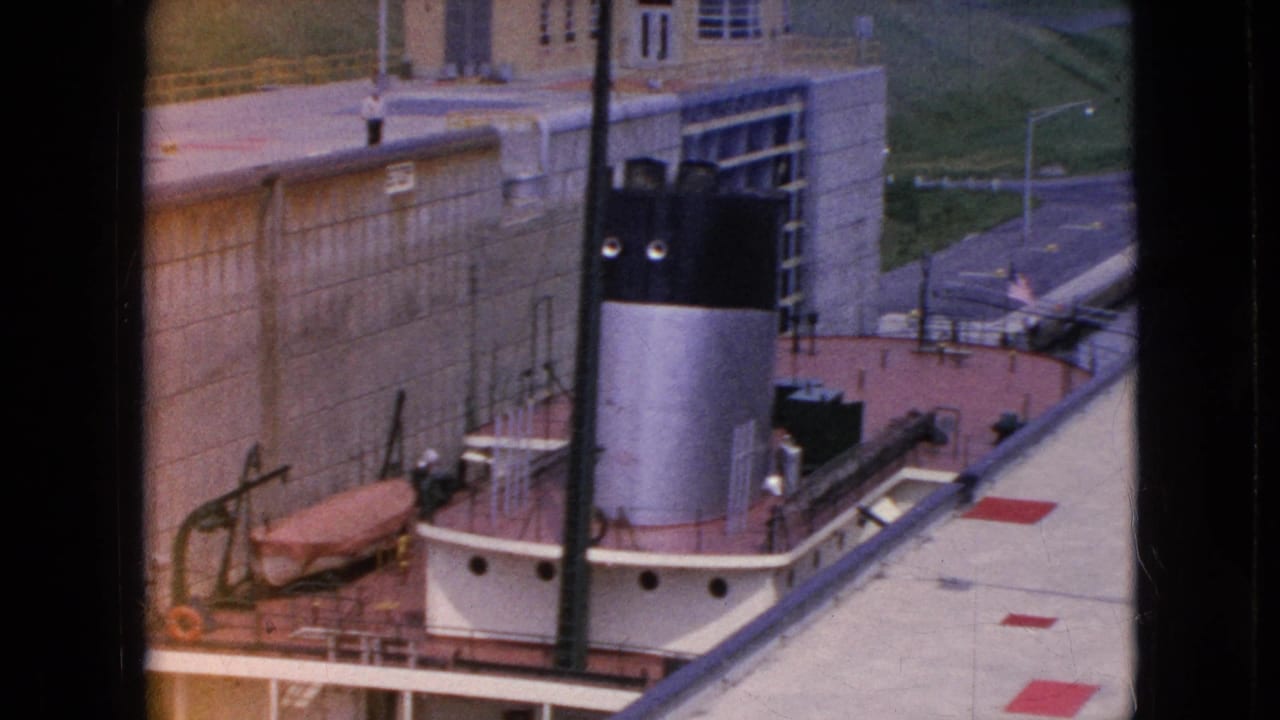 High-angle view of a boat deck, smokestack, lock wall, and canal-side road.