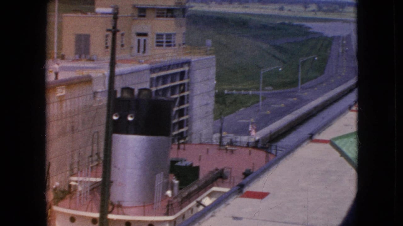 1964 8mm frame from Niagara Falls, New York, showing a large tug or workboat entering a concrete canal lock with a control building and grassy embankment beyond.