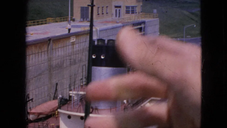 A foreground hand points across 1964 home-movie footage of a ship beside a tall concrete lock wall at Niagara Falls, New York.