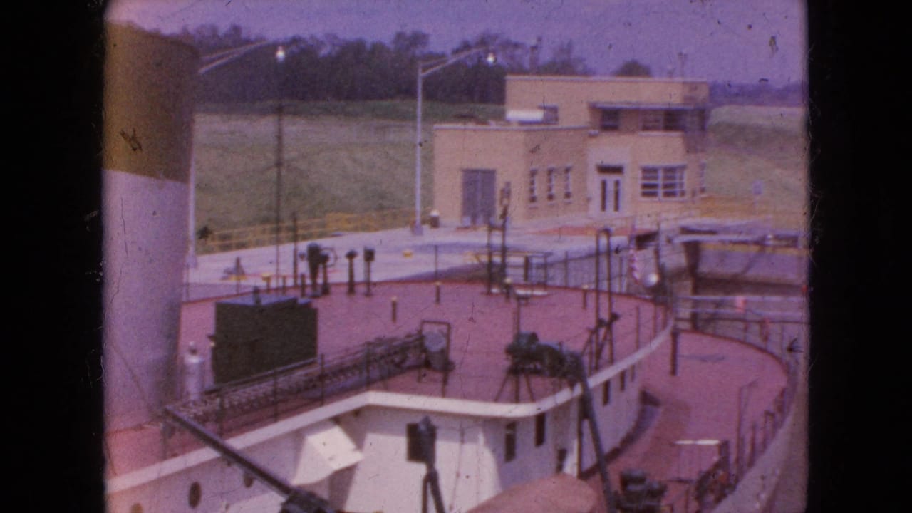 Vessel deck and railings beside a tan lock control building and grassy embankment.