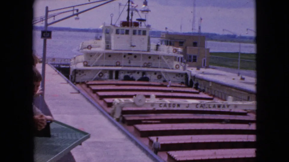1964 Niagara Falls, New York frame showing the CASON J. CALLAWAY in a lock, with a partial visitor figure at the foreground edge and dockside infrastructure around the vessel.