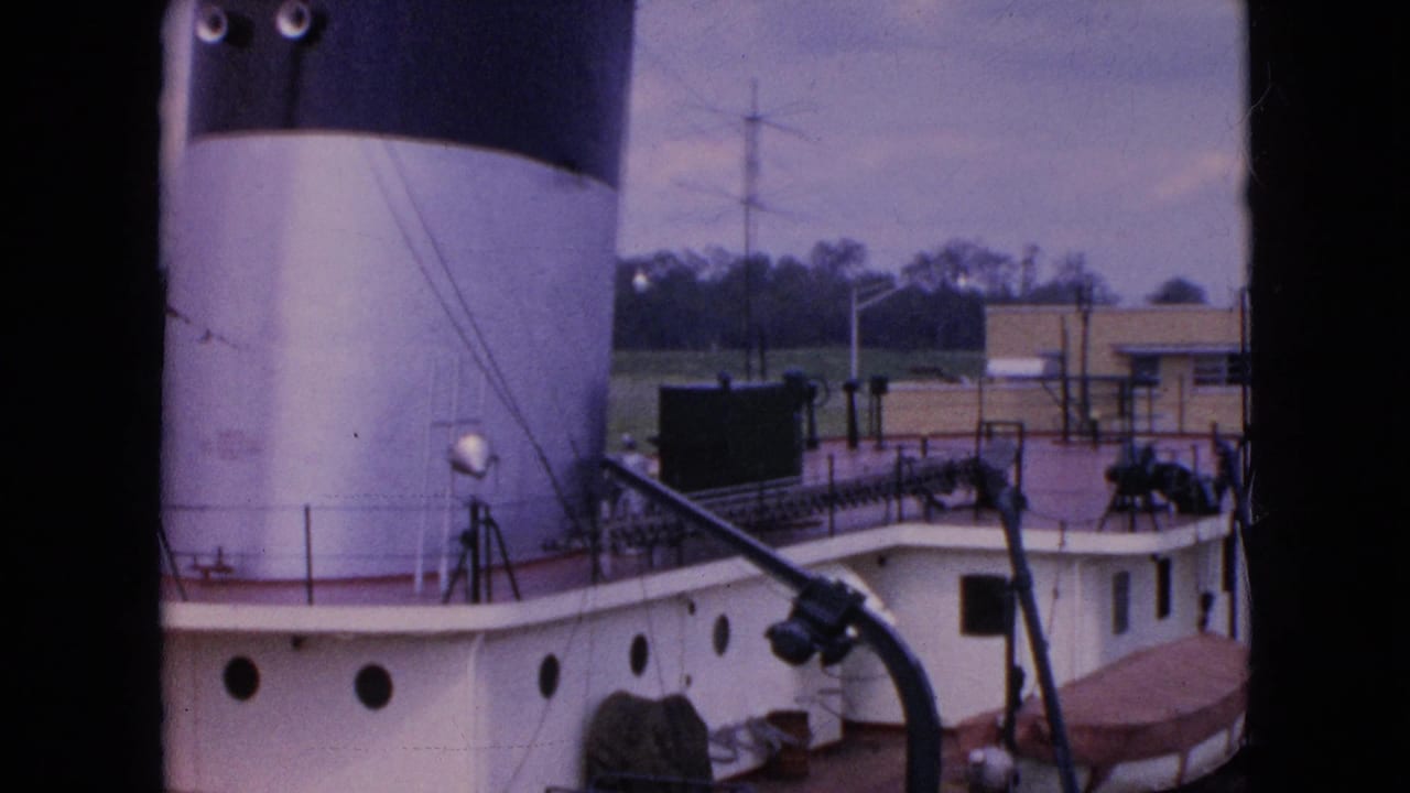 1964 Niagara Falls home-movie frame looking down at a docked white and brown riverboat deck with a large smokestack, railings, and equipment visible.