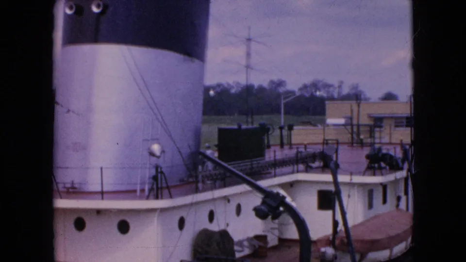1964 Niagara Falls home-movie frame looking down at a docked white and brown riverboat deck with a large smokestack, railings, and equipment visible.