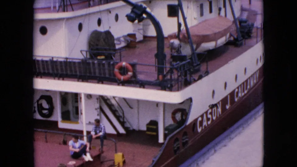 1964 Niagara Falls frame of the docked Cason J. Callaway seen from above, showing two men seated below the deck, a life preserver, covered lifeboat, and partial vessel lettering.