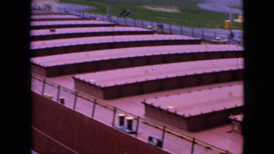 The frame concentrates on the freighter's reddish hatch covers and side railings, with a small visible person or figure near the upper deck or dock area and grass beyond.