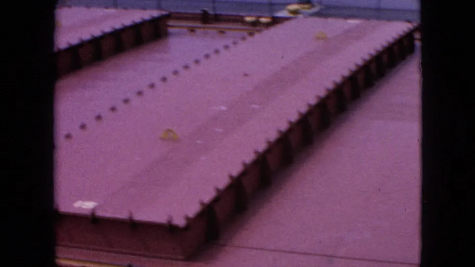1964 Niagara Falls 8mm frame showing a closer elevated view of a long reddish flat roof, repeated edge details, railings, and adjacent paved space.