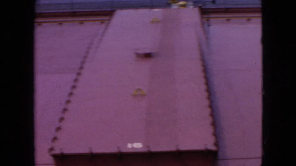 Final 1964 Niagara Falls frame looking down at a broad reddish industrial roof with rows of small raised points, a central roof fixture, and surrounding pavement.