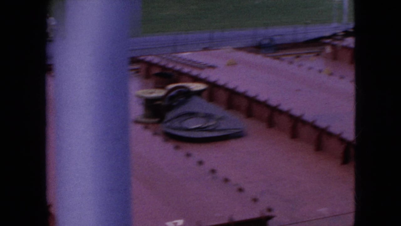 Red tanker deck with a dark hatch or cover and coiled line near the rail.