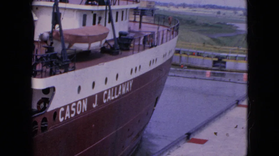 Bow-side view of the Cason J. Callaway in 1964 footage, showing the vessel name in large lettering, red-brown hull paint, upper railings, and nearby lock or dock surfaces.