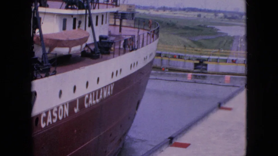 The Cason J. Callaway passes through or alongside a lock or dock area in the 1964 Niagara Falls, New York footage, with hull lettering, railings, cranes, and paved waterway edges visible.