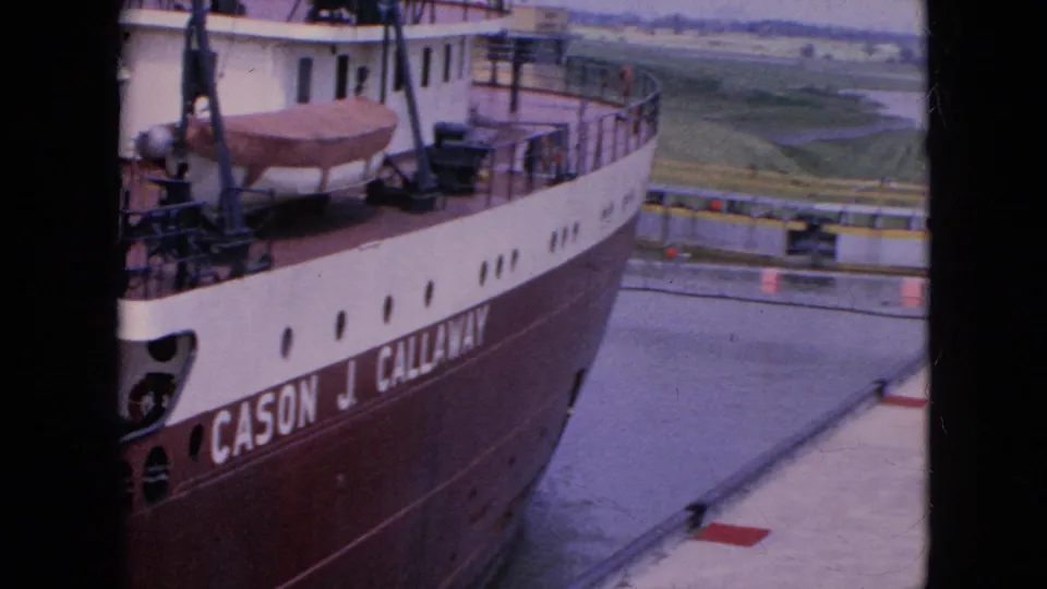 Close 8mm view of the Cason J. Callaway freighter in the lock, with the ship name partly readable, deck railings, a covered lifeboat, water, and green land beyond the lock.
