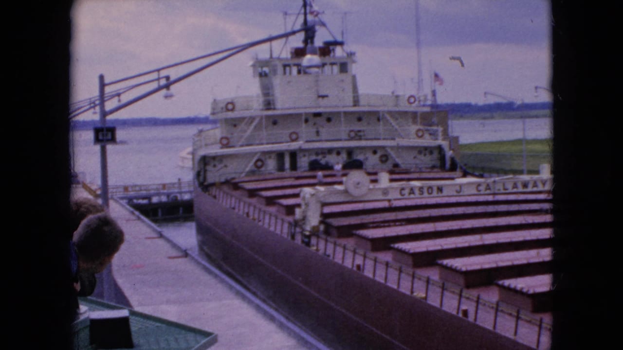 Freighter stern and open cargo holds waiting in a lock, with a person partly visible in the foreground.