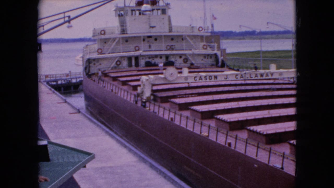 Docked cargo ship viewed from above with its name painted along the side and water behind it.