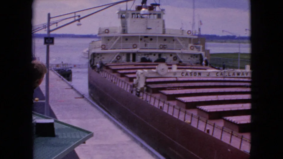 1964 United States 8mm frame showing the CASON J. CALLAWAY freighter from a slightly elevated dock-side angle, with a spectator partly visible in the foreground.