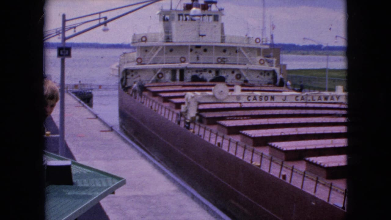 Large cargo freighter docked beside a concrete pier with a partial person at the left edge.