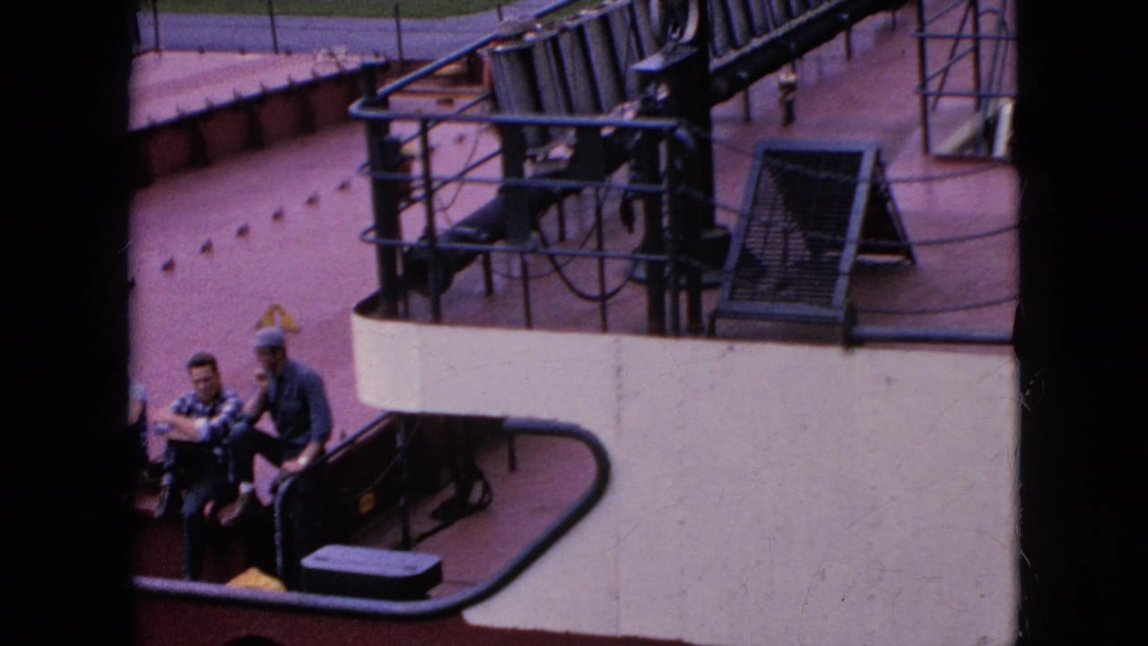 Two men sitting beside railings on a red-and-white boat deck.