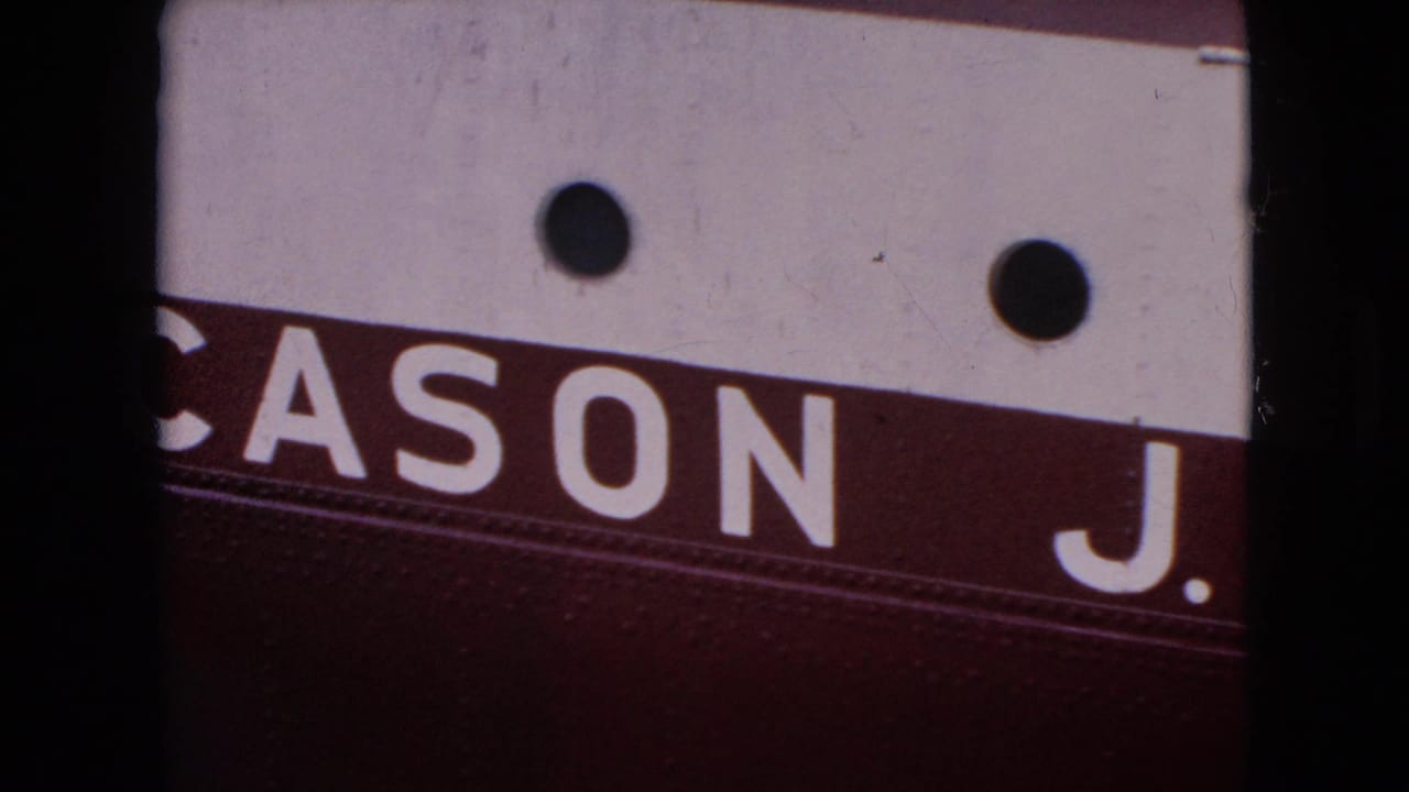 Close 1964 8mm frame showing the letters “CASON J.” in white on a burgundy stripe below a white painted panel with two dark circular fittings.