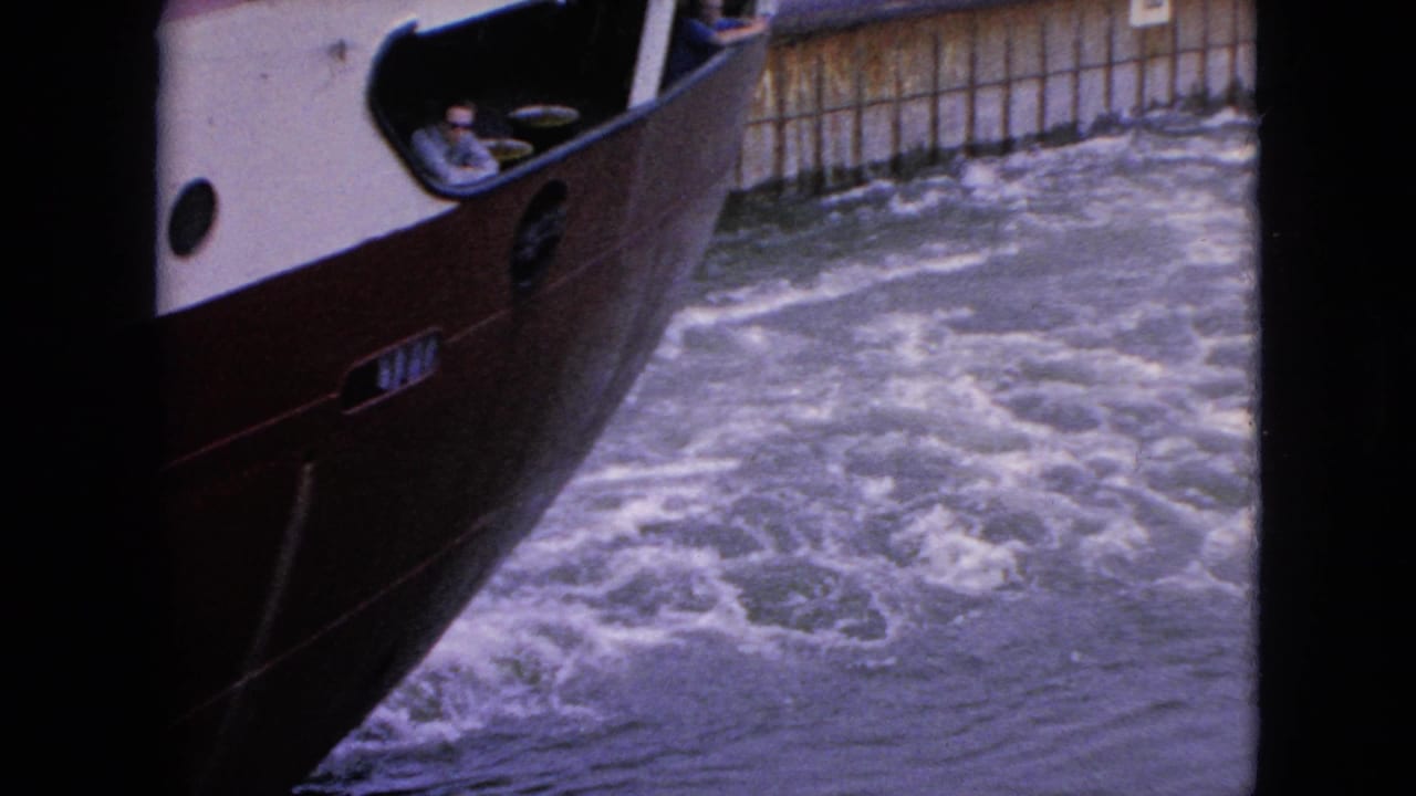 Boat bow and cabin pass along foamy water near a wooden wall.