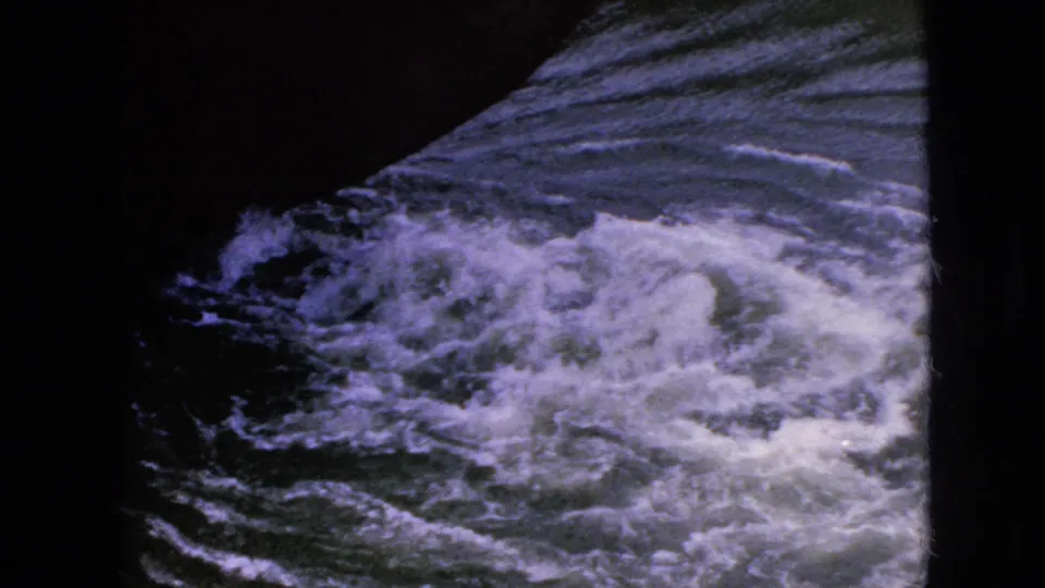 Turbulent water at a waterways setting, likely from the Niagara Falls travel footage, filmed through a dark structural or window-like frame on 8mm film.