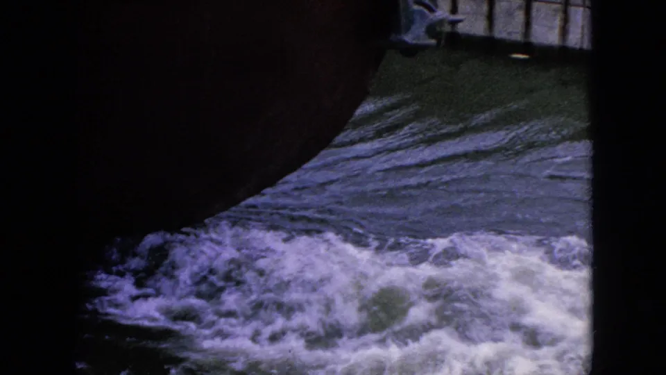 Foaming water rushes past a dark foreground shape, continuing the visitor-shot Niagara Falls area waterways view from the 1964 8mm footage.