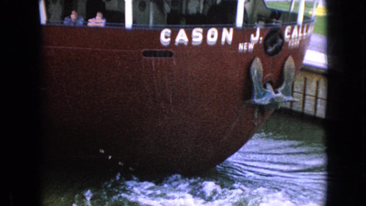 Bow area of red boat with vessel lettering, anchor hardware, and wake at the dock.