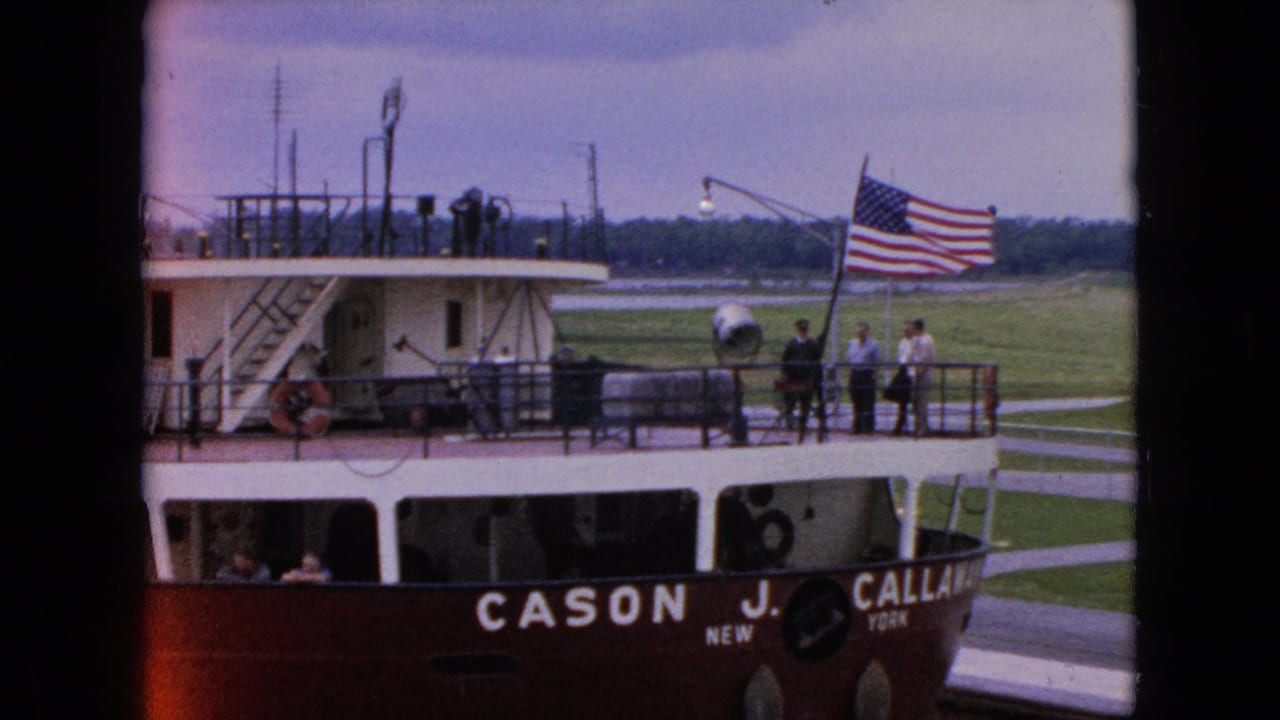 1964 8mm frame of the Cason J. Callaway beside a harbor edge in the Niagara Falls, New York area, with passengers on deck and an American flag at the stern.