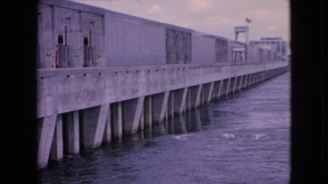 Long concrete dam receding into the distance with water moving alongside it.