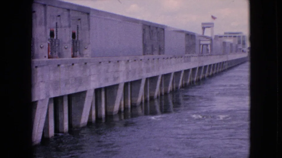 1964 Niagara Falls hydro dam view with the concrete structure extending across the frame and water flowing beneath its support pillars.