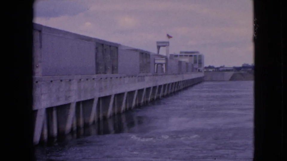 The Niagara Falls, New York infrastructure view continues, with the concrete wall receding into the distance and water moving beneath the structure in soft 8mm color.