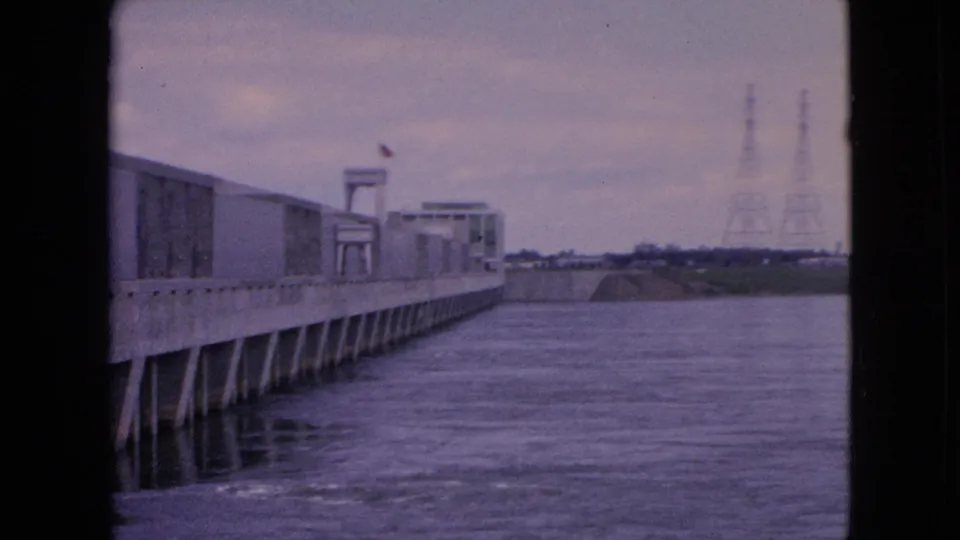 Wide 8mm view of the concrete river structure, moving water, distant shoreline, and utility towers in the Niagara Falls, New York area.