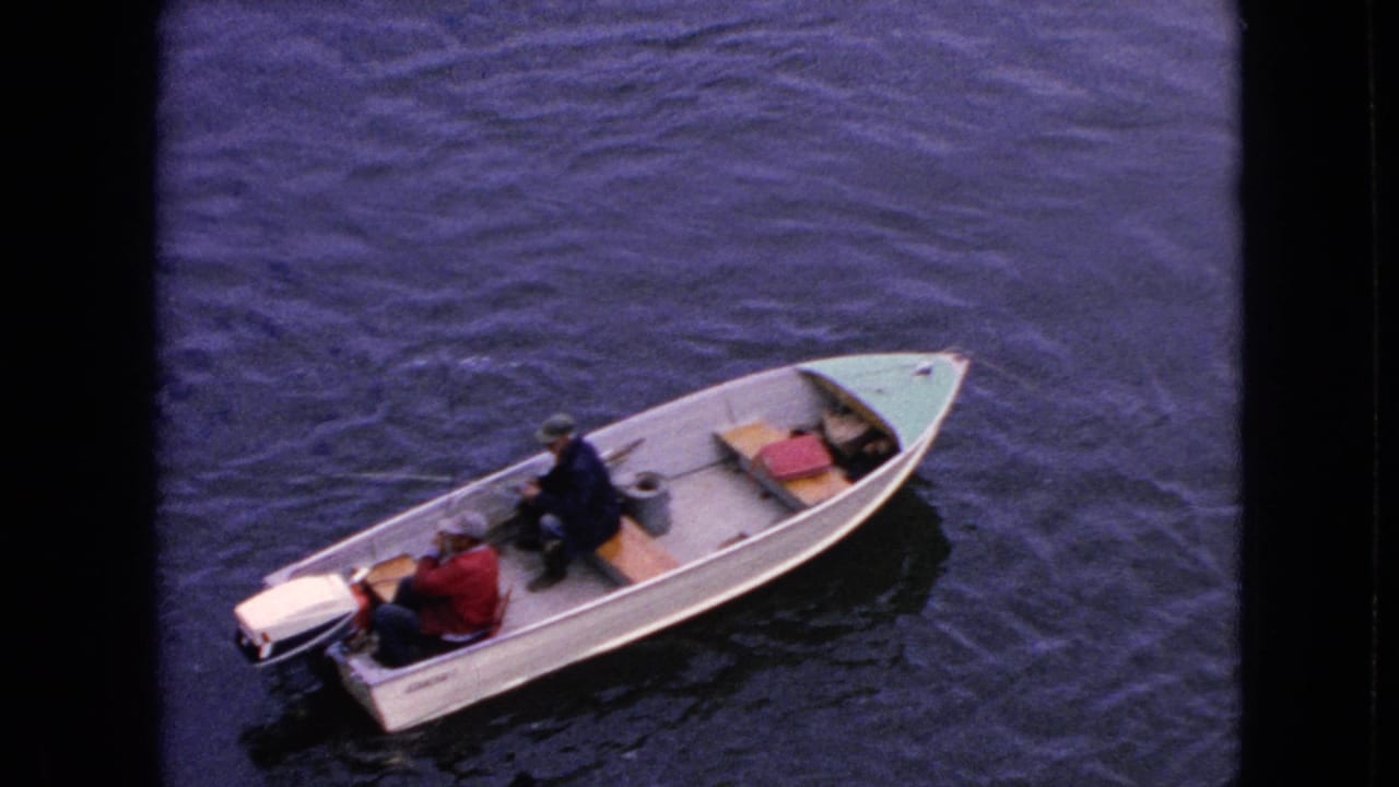 Small motorboat with two men seen from above on rippling water.