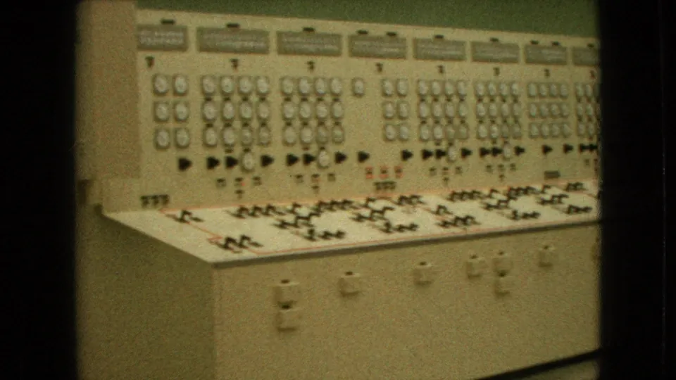 1964 Niagara Falls home-movie frame showing an analog industrial control panel with rows of circular gauges, switches, labels, and a slanted console surface.