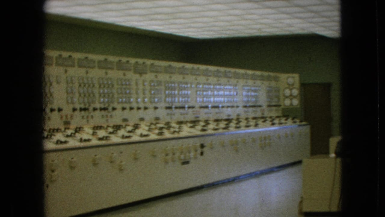 Wide control console stretching across a green-walled room with analog panels and floor space.