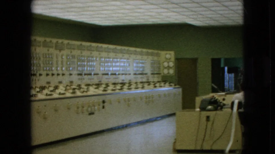 The control room view widens to include the analog console, a nearby desk with a telephone, a chair, and a doorway along the green wall.