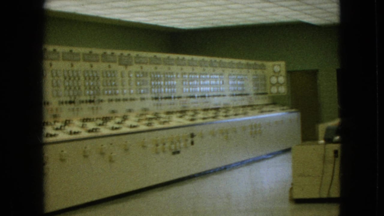 1964 8mm frame from Niagara Falls, New York, showing a long beige computer-era control console with rows of switches, lights, and gauges in a green-walled interior.