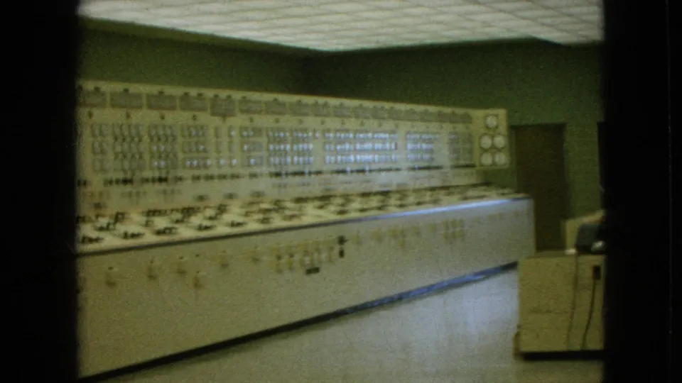 1964 8mm frame from Niagara Falls, New York, showing a long beige computer-era control console with rows of switches, lights, and gauges in a green-walled interior.