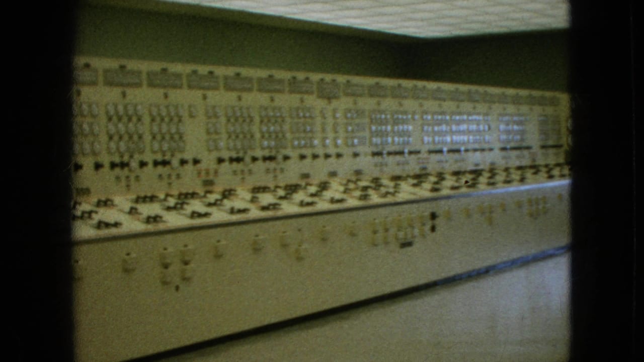 Wide control-room panel stretching across the frame with many switches and lights.