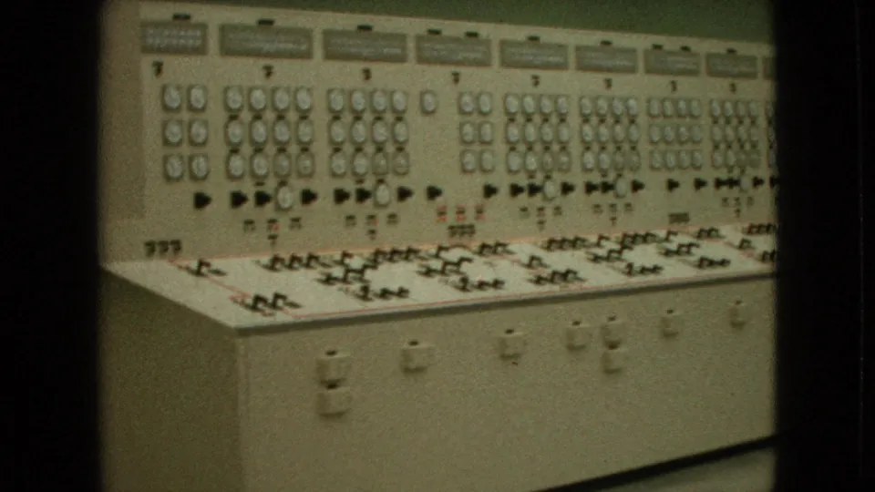 1964 8mm frame showing a hydroelectric-style electrical control panel with analog gauges, toggle switches, indicator lamps, and labeled sections.