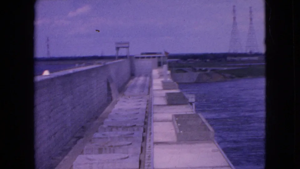 Final exterior frame from the Niagara Falls, New York footage showing the water barrier, concrete walkway, broad water channel, and distant utility structures.