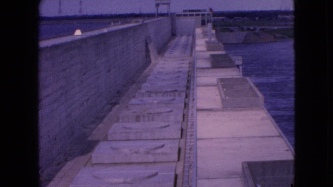 Long concrete walkway with repeating blocks, railing, and water at right.