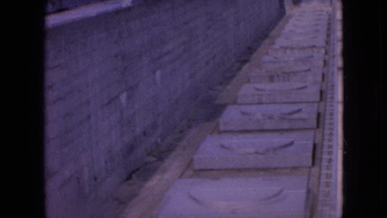 1964 Niagara Falls home-movie frame showing rectangular concrete slabs beside a high stone wall, with the view looking down along a narrow construction passage.