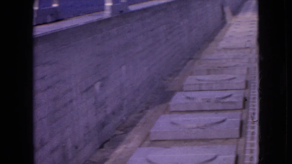 1964 Niagara Falls footage frame with an angled view down a stone-walled channel where rectangular concrete slabs appear laid in sequence.