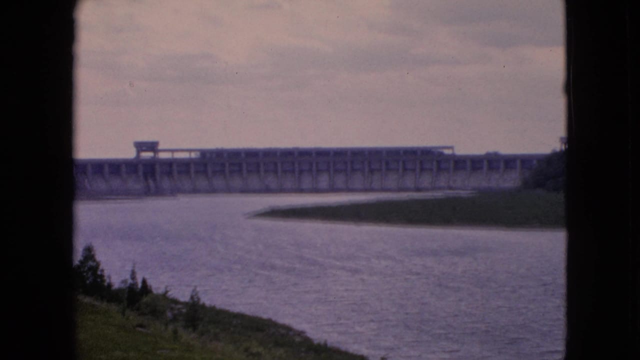 Concrete dam and rippled river seen past a dark vertical foreground edge.